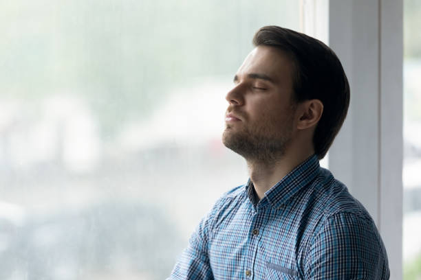 istock Close up mindful man with closed eyes meditating near window 1372744127