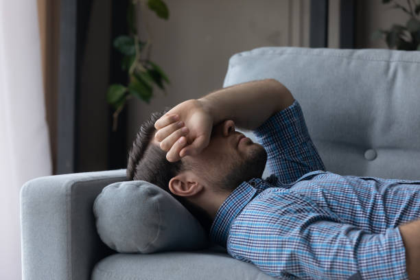 Sick man feeling headache or dizziness, lying on couch Sick man feeling headache migraine or dizziness, covering eyes with hand, lying on couch at home, exhausted tired millennial male sleeping after difficult working day, resting on comfortable sofa narcolepsy stock pictures, royalty-free photos & images