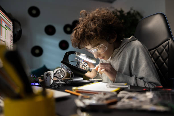 istock Little boy with safety glasses, future electronics technician, learning how to solder microprocessor cables and printed circuits, looking through a magnifying glass, repairing and testing electronics 1372751770