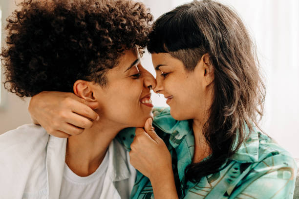 Playful lesbian couple touching their noses together Playful lesbian couple touching their noses together at home. Two affectionate female lovers flirting with each other. Romantic young lesbian couple sitting together in their living room. lesbian stock pictures, royalty-free photos & images