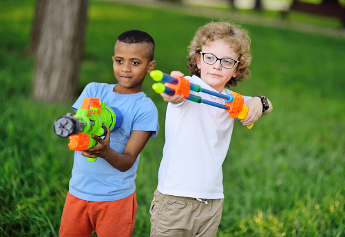 two children of a boy with toy guns are smiling in a park against a background of greenery. Children's games