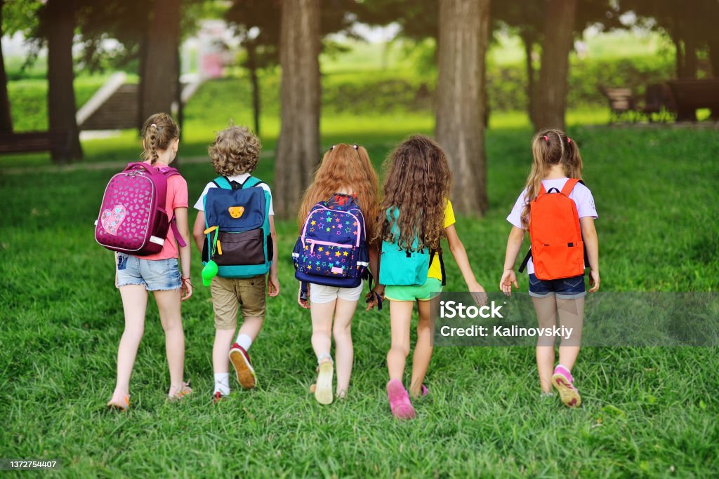 group of children with school backpacks walking hand in hand. Holidays, back to school, summer camp Rear view - a group of children with school backpacks walking hand in hand. Holidays, back to school, summer camp. Summer Camp Stock Photo