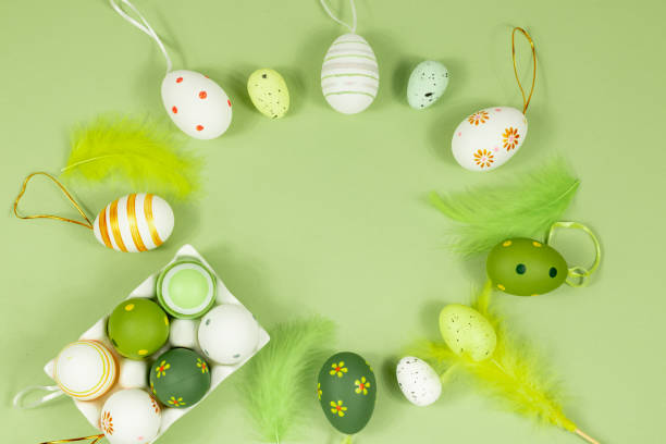 istock Top view of Easter eggs in an egg stand, painted with different patterns and feathers on a green background. Copy space. Place for an inscription. 1372756913
