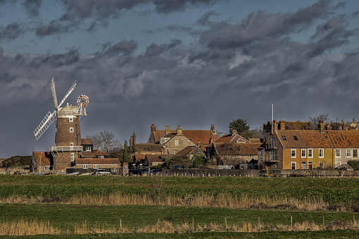 Cley Windmill landscape Rural view across North Norfolk UK. High-contrast image of the pretty coastal village of Cley-next-the-sea. Retro windmill with storm cloud painterly sky over agricultural land