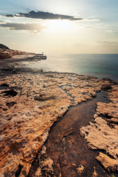 A man standing on a rocky coast in Akyar, Mersin Province in Turkey on an afternoon in February 2022.