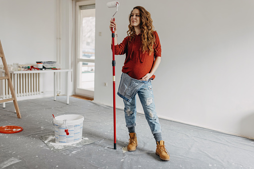 Young pregnant woman painting nursery room