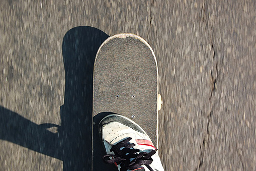 Top view of a skateboard and one foot moving on the asphalt on a sunny day. Skateboard and foot centered. Space for text. Skateboard concept. Skateboarder concept.