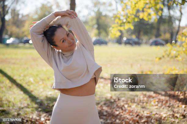 Woman In Casual Sports Clothes Stretching Arms And Smiling At Camera Leisure Activity Outdoors Stock Photo - Download Image Now