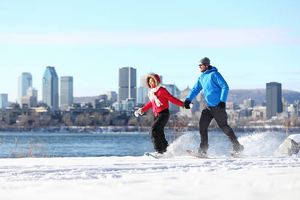 couple snowshoeing in montreal Winter fun couple on snowshoes running with montreal cityscape skyline and river st. Lawrence in background. Healthy lifestyle photo from Montreal, Quebec, Canada. montreal stock pictures, royalty-free photos & images