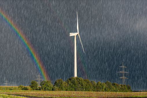 A wind turbine in front of a dark sky during a storm with raindrops and rainbows