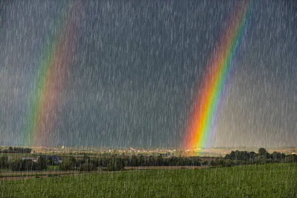 A rainbow with a side rainbow on the horizon during a storm with raindrops and gray sky