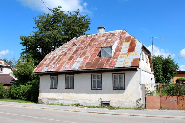 錆びた金属屋根のタイルで覆われたひび割れたファサードを持つコンクリート基礎の農村地域の伝統的な小さな古い家族の家 - next to ストックフォトと画像