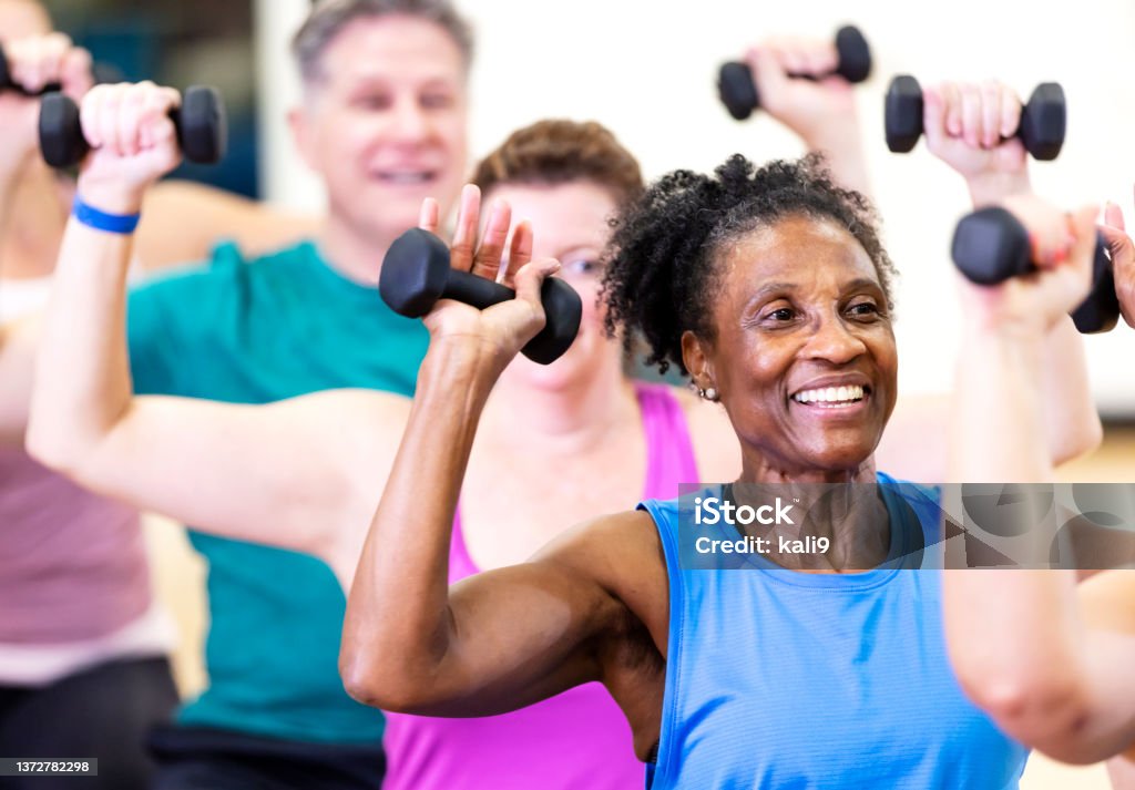 Senior African-American woman in exercise class Close-up of a senior African-American woman in her 60s enjoying an exercise class. She is with a multiracial group of mature adults sitting on fitness balls and lifting hand weights. Exercising Stock Photo
