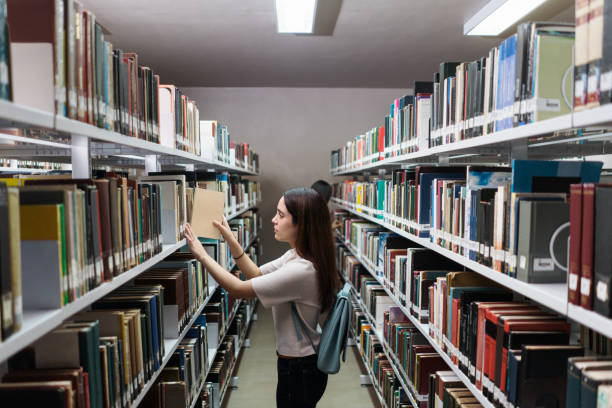 istock Female student picking book from bookshelves at library 1372784180