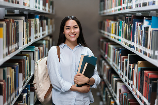 A happy female student standing in the library and smiling at the camera.