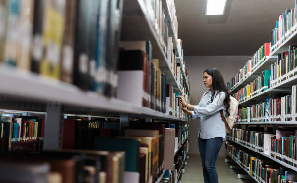 istock Female student looking for book in library 1372784280