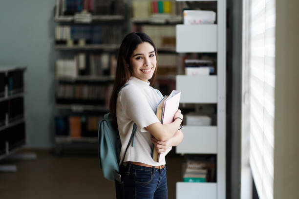 istock Female student standing by window at library and smiling 1372785697