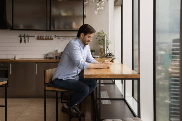 istock Millennial male sit in modern kitchen using smartphone 1372788105