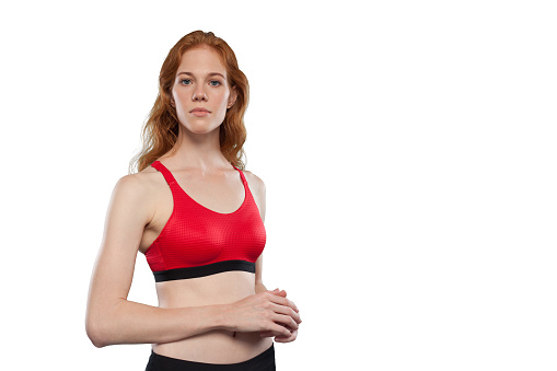 Female athlete poses on a white background. Studio portrait of woman wearing red sporty tank top. Being like hero look