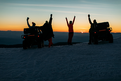 Group of friends having good time on mountain peak with snow vehicles