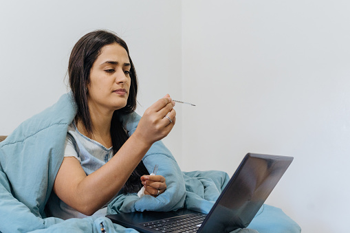 Mujer con fiebre en videollamada en portátil photo