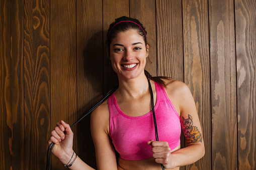 Smiling fit young woman holding a jumprope while standing in her workout studio