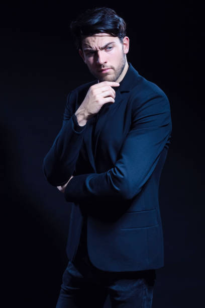 istock Thinking Caucasian Brunet Man In Black Suit Posing With Folded Hands Looking To Side Over Dark Background in Studio. 1372796494