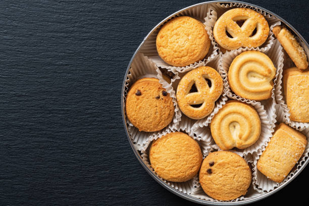 istock Set of crispy shortbread biscuits in an open tin over black slate surface. Tasty danish butter cookies in can for breakfast. Baked pastry, sweet food and calories concepts. Copy space. 1372797135