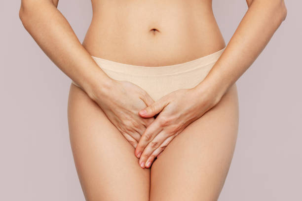 young woman in underwear holding her crotch with hands, suffering from cystitis on beige background - roupa de baixo imagens e fotografias de stock