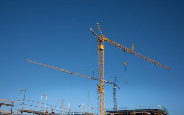 istock Two yellow construction cranes stand out against a blue sky at a residential construction site. At the bottom edge of the picture is a section of the building shell. 1372800320