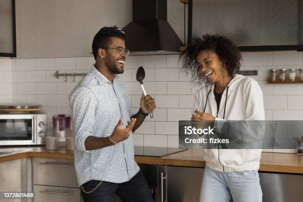 Happy young African American couple singing songs in kitchen.