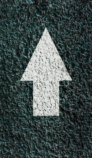 White pointing arrow on a textured asphalt surface. Direction icon.