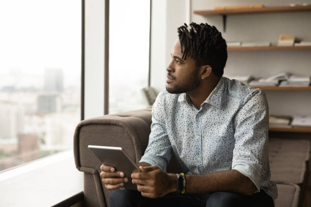 istock Dreamy thoughtful young African man holding digital tablet. 1372801813