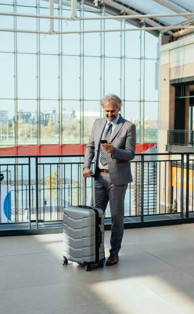 istock Smiling Business Man with Suitcase Using Mobile Phone While Standing at the Airport 1372809063