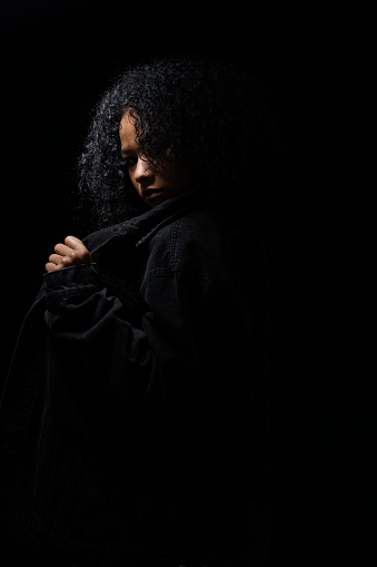 Latin woman of average age from 20 to 29 years of age with Afro hair and skin is dressed all in black with a black background and is photographed in portraits