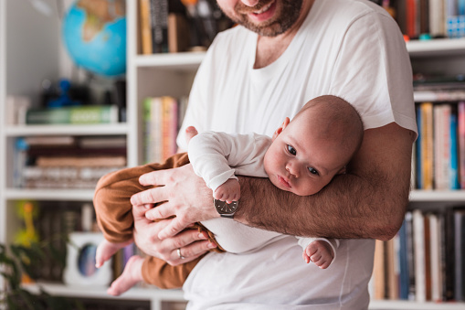 Happy man smiling when holding a baby boy in his hands at home