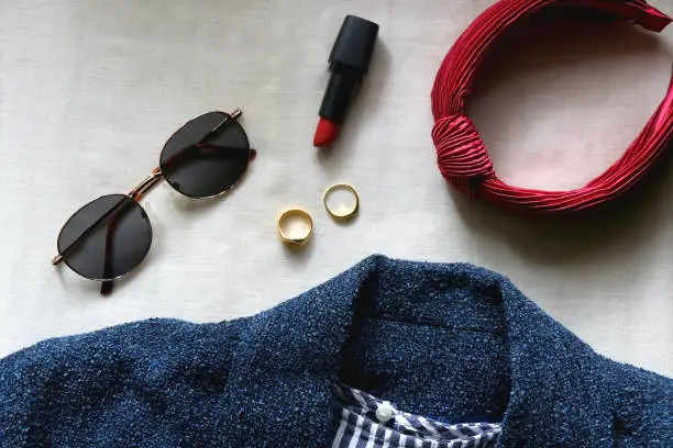 Blue jacket, striped shirt, round sunglasses, red hair band, red lipstick and gold rings. Flat lay.