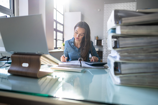 Young Businesswoman Working At Office With Stack Of Folders On Desk