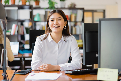 Portrait of an asian young businesswoman sitting at her desk. Confident female professional looking at camera and smiling.