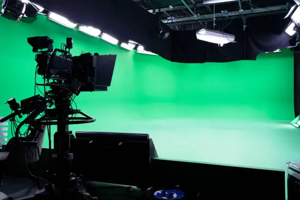 Photo of The camera on the tripod, led floodlight, spotlight, prompter and a monitor on a green background. The chroma key. Green screen. Broadcast industry