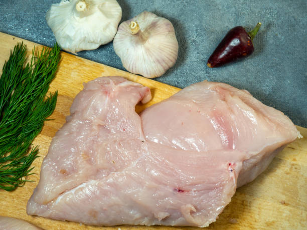 istock Chicken breast fillet pieces on a cutting board. Still life on a black background. Multi-colored peppercorns, dill, hot pepper and garlic around a piece of meat. 1372841922