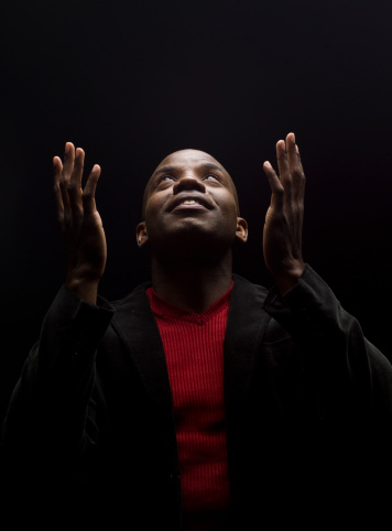 young afro caribbean male praying on black background (this picture has been taken with a Hasselblad H3D II 31 megapixels camera)