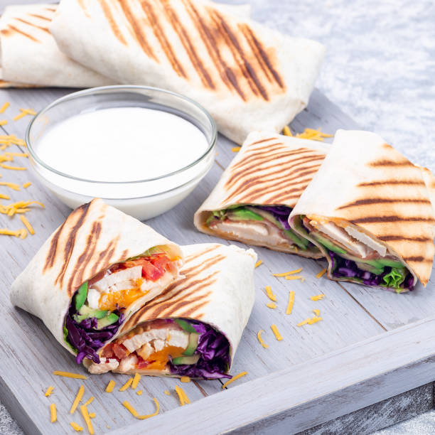 istock Chicken wraps with red cabbage, avocado, tomato, lettuce, cheddar cheese, on wooden tray, square 1372844629