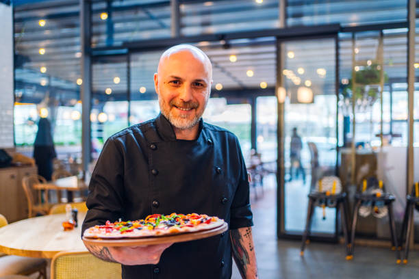 smiling waiter looking at camera and showing a pizza - pizzeria imagens e fotografias de stock