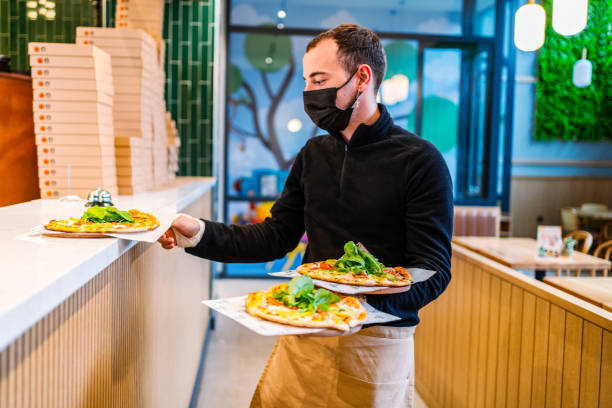 istock Smiling waiter looking at camera and showing a pizza 1372853227