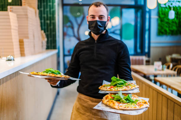 istock Smiling waiter looking at camera and showing a pizza 1372853542