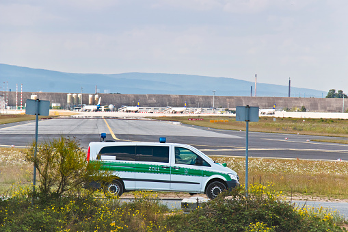 German customs officials secure an outside area of the airport with a vehicle. In this area, planes cleared by customs are parked, departing the next day.\nThis image is part of an airport series.