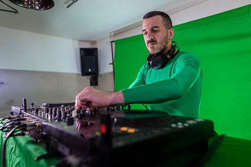 Caucasian DJ, with cool attitude, playing music set, in front of the green screen, wearing green suit, while recording the music video