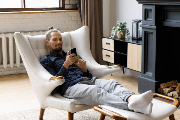 istock Happy relaxed young hipster man using cellphone, sitting in armchair. 1372859403