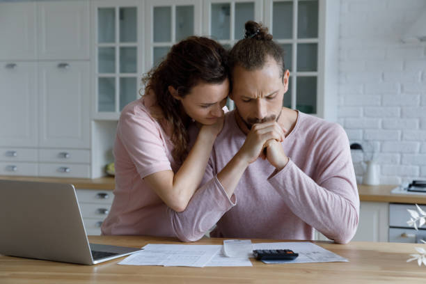 Unhappy young family couple having financial problems. Unhappy young woman supporting stressed husband, feeling depressed having financial problems, calculating bills, planning budget together at home, suffering from lack of money, bankruptcy concept. cost of living stock pictures, royalty-free photos & images